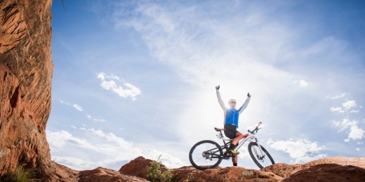 Mountain biker on top of on rock with arms raised